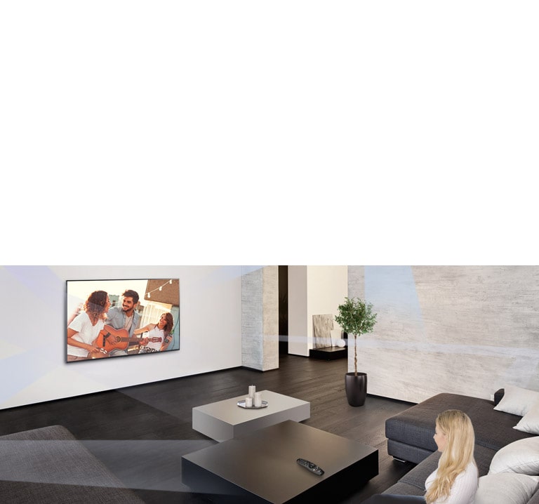 امرأة تجلس في غرفة معيشة رحبة تتميز بديكور داخلي بسيط وتشاهد أشخاصًا يلعبون على شاشة التلفزيون