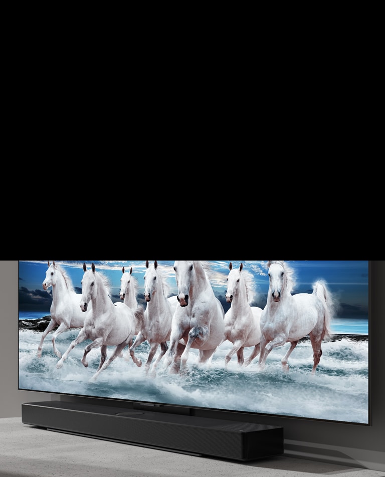 Sound bar and TV are placed on the white table and 7 white horses are shown on the TV.