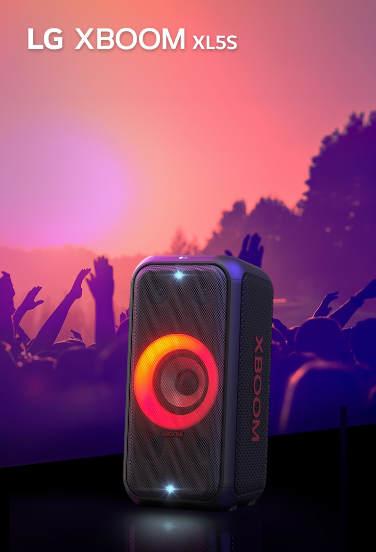 LG XBOOM XL5S е поставен на сцената с включени светлини в преливащи се червени и оранжеви цветове. Зад сцената хора се наслаждават на музиката.