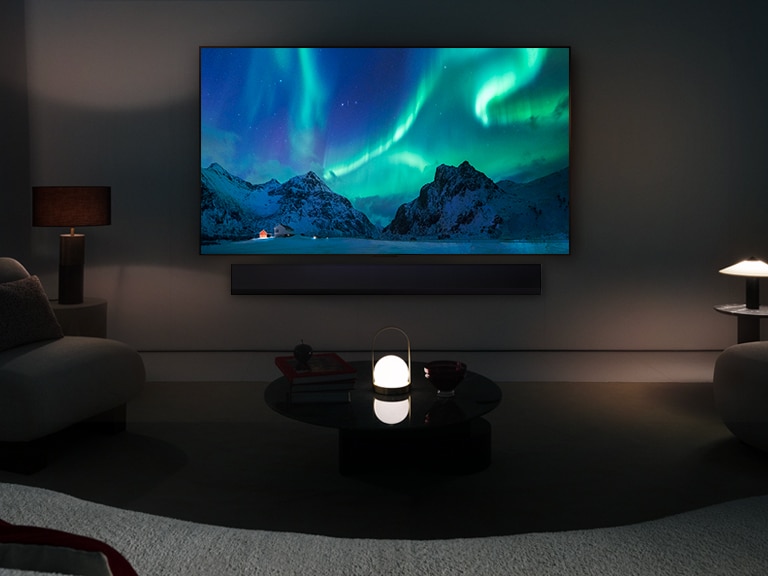 TV OLED LG et la barre de son LG dans un espace de vie moderne pendant la nuit. L’image à l’écran des aurores boréales s’affiche avec des niveaux de luminosité idéaux.