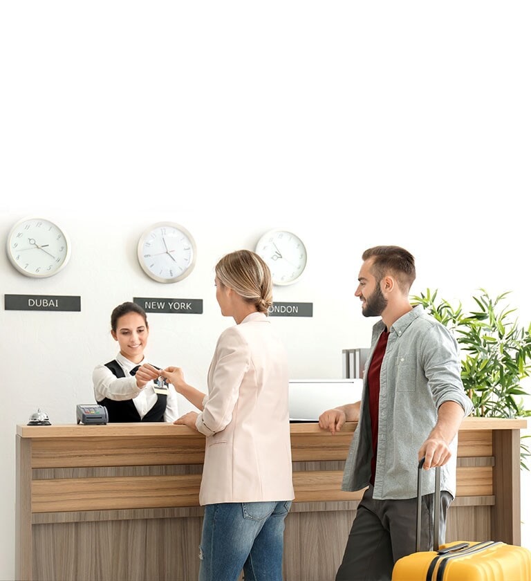 Uma imagem de um casal a fazer check-in com uma rececionista no átrio de um hotel.