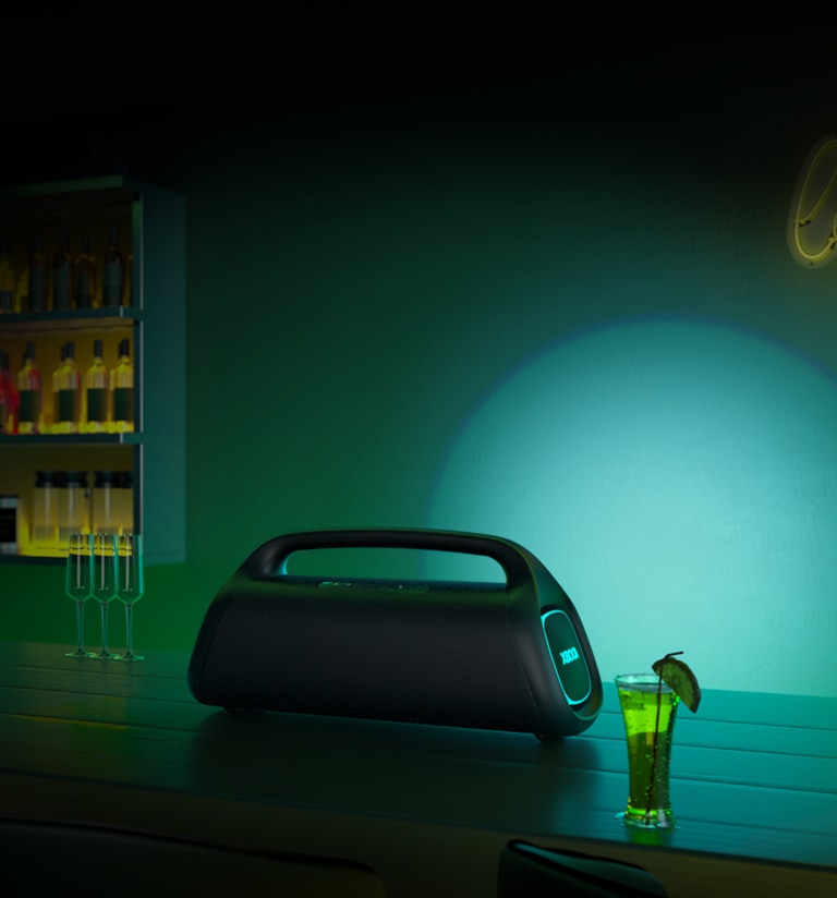 A LG XBOOM GO XG9 está colocada na mesa do bar. Ela projeta uma iluminação de palco verde e azul.