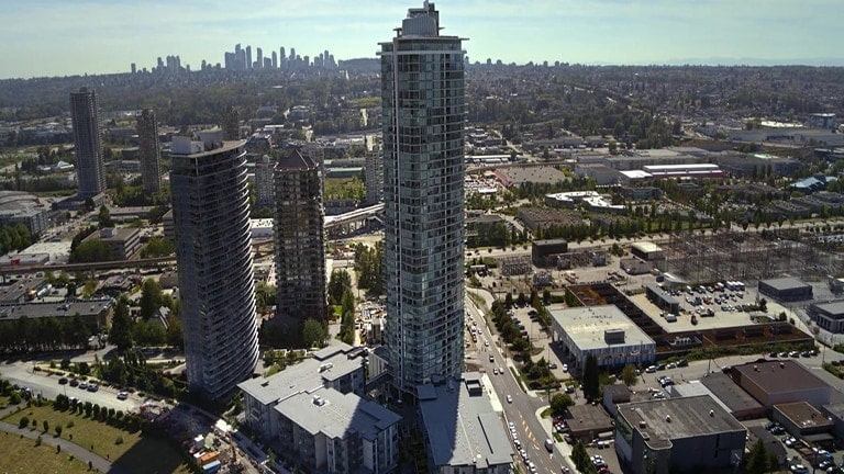 À luz do dia, a vista de uma megacidade revela um edifício alto e redondo de vidro no centro, ladeado por edifícios mais baixos à esquerda, sob um céu azul nublado.