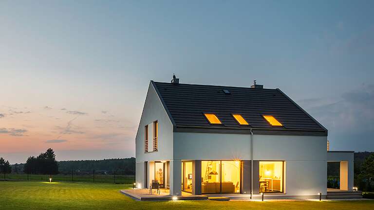 No meio de uma exuberante área gramada, uma grande casa branca com telhado preto emana luz, iluminando de forma brilhante a paisagem circundante.
