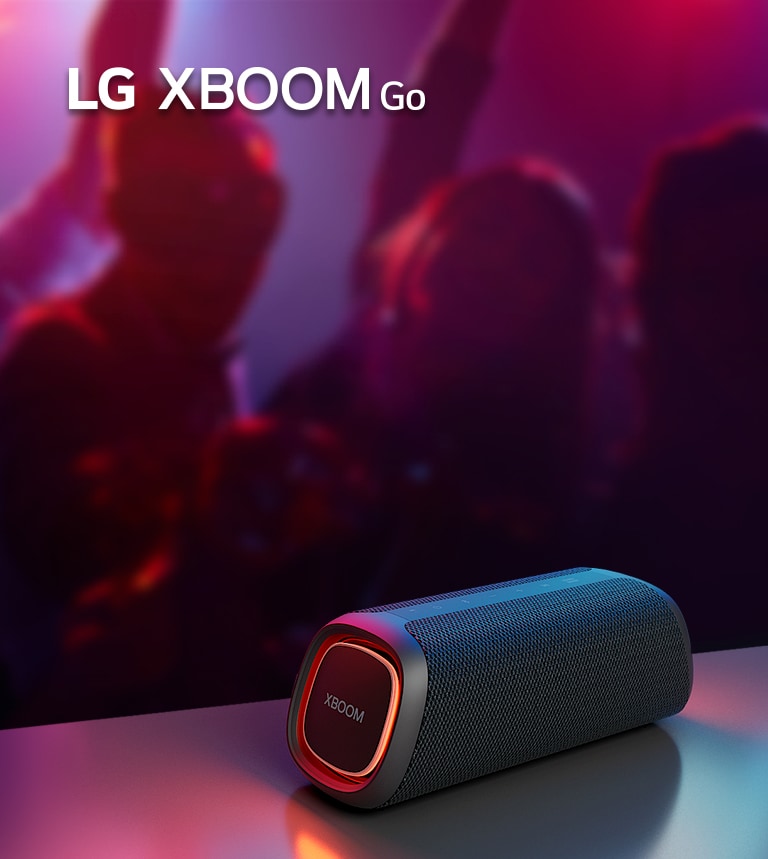 A LG XBOOM Go XG5 está disposta numa mesa metálica com a iluminação laranja ligada. Atrás da mesa, pessoas dançam ao som da música.
