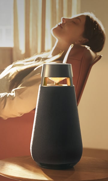 Eine Frau entspannt sich in einem Sessel und hört über einen XO3-Lautsprecher Musik.
