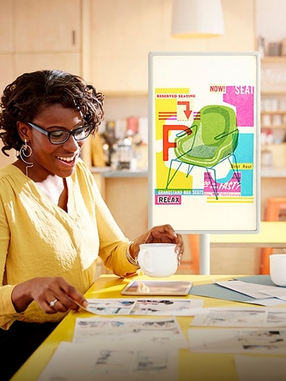 放置在辦公室的 StanbyME 螢幕上顯示著椅子的設計圖像，一名女性正在開會，她正在看報紙。