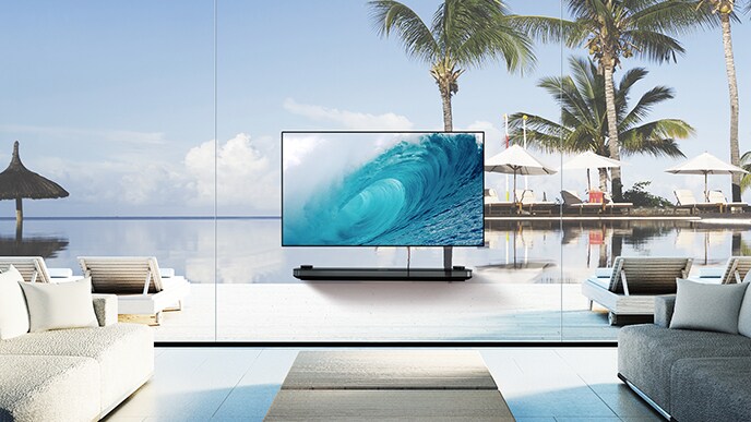 LG SIGNATURE OLED TV W躺在客廳裡，窗外展示著藍色的海景，在屏幕上顯示涼爽的波浪。