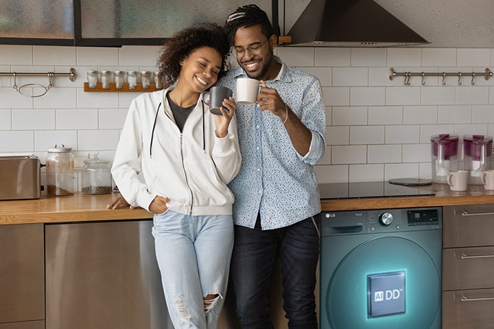 Пара, держащая чашку, стоит рядом со стиральной машиной. Из стиральной машины выходит линия искусственного интеллекта с логотипом AIDD и обнаруживает их одежду.