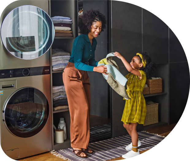 A woman and a young girl standing in front of a washing machine, holding clothes.