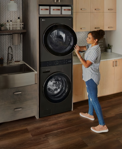 A woman standing in front of an LG washing machine and dryer, preparing to do laundry.