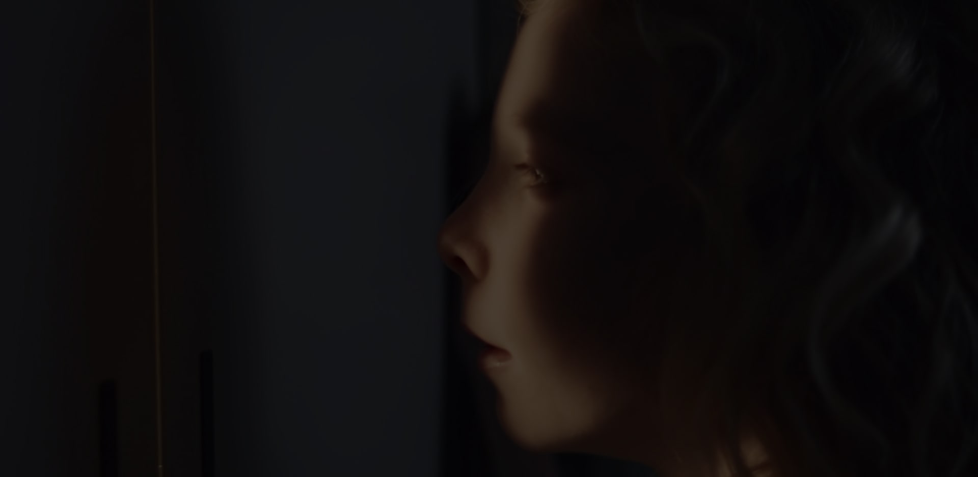 Eine Nahaufnahme vom Gesicht eines Mädchens, das sich zum Teil im Schatten, zum Teil im Licht befindet, während es aus seinem Versteck blickt.