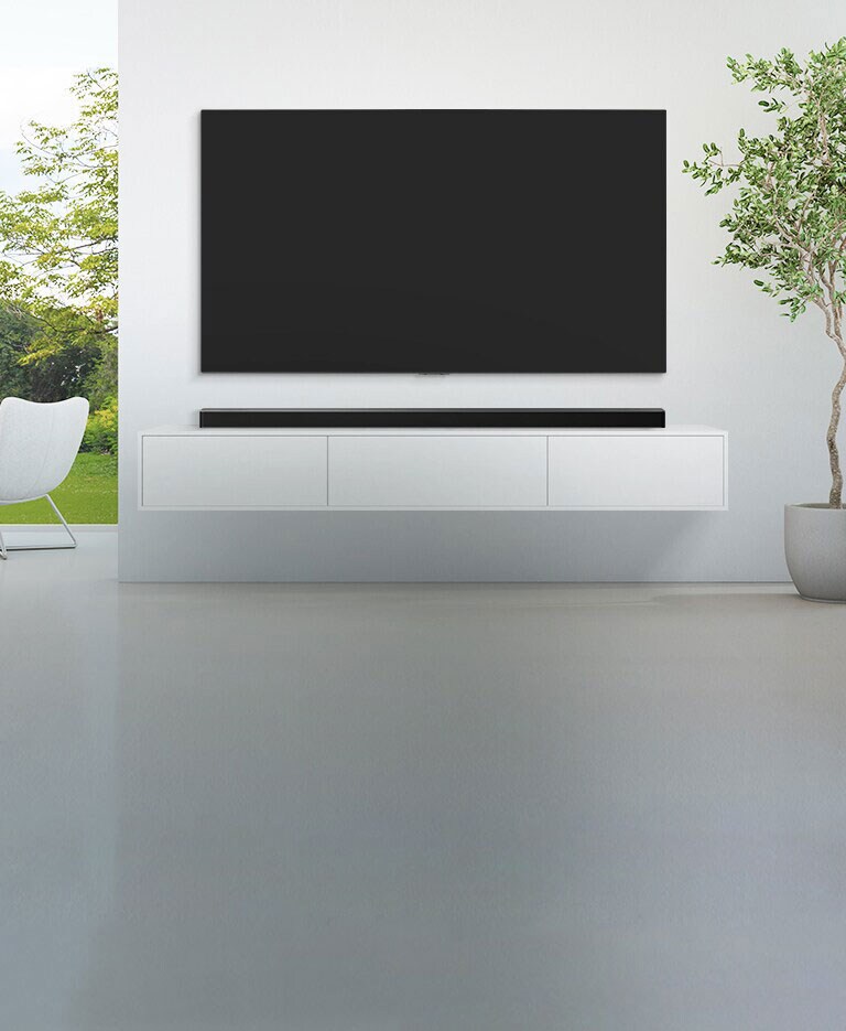 Televisio ja soundbar on sijoitettu suureen, valkoiseen olohuoneeseen, ja sen leveästä ikkunasta on näkymä vihreään metsään. 