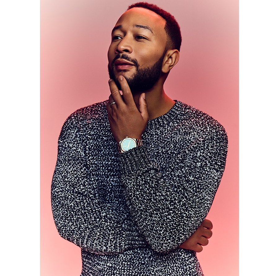 Picture of John Legend touching his chin against a red background.