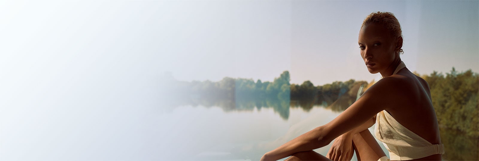 Image of a model wearing one of the Winter Sun capsule collection pieces sitting  in front of a beautiful lake