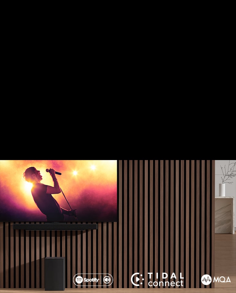 LG OLED C תלויה על הקיר, מתחתיה, מקרן הקול SC9S מבית LG מותקן באמצעות התושבת הבלעדית. הסאב וופר ניצב מתחתיו. בטלוויזיה מוצגת הופעה חיה.