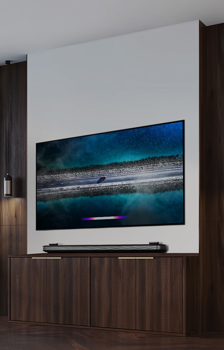 LG SIGNATURE OLED TV W9 روی دیوار آویزان شده است و یک تخت درست در مقابل تلویزیون با آسمان آبی بالای پنجره قرار گرفته است.			