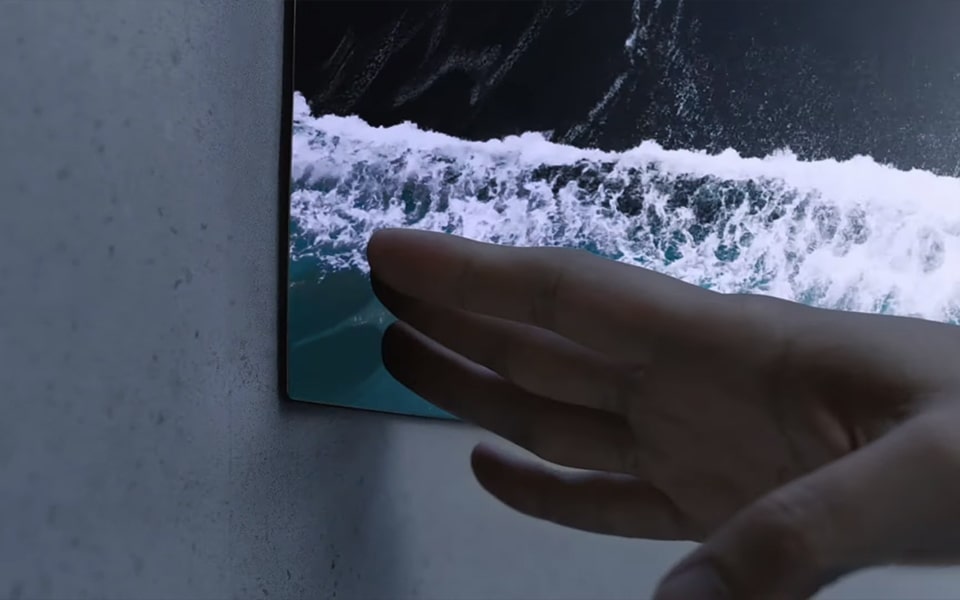 Dłoń dotyka ultracienkiego telewizora LG OLED.