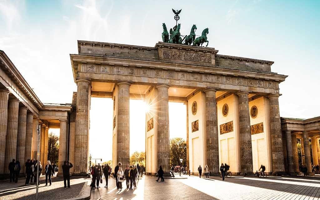 Podróżuj po Berlinie: słońce świeci przez Bramę Brandenburską, podczas gdy ludzie przechodzą przez bramę w Berlinie, Niemcy.