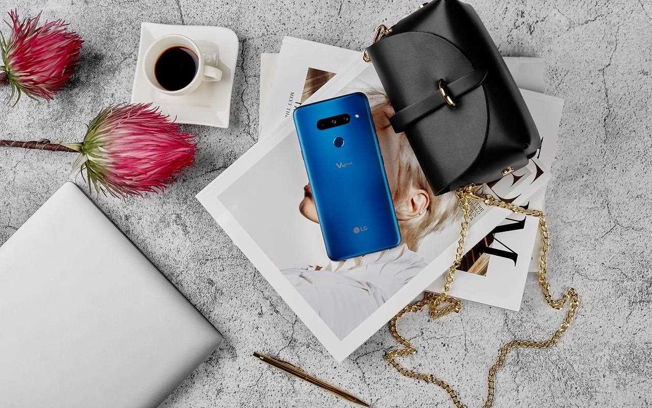 Niebieski, elegancki smartfon V40 leżący na magazynach z modą, obok skórzanej torebki, kwiatów i filiżanki z kawą