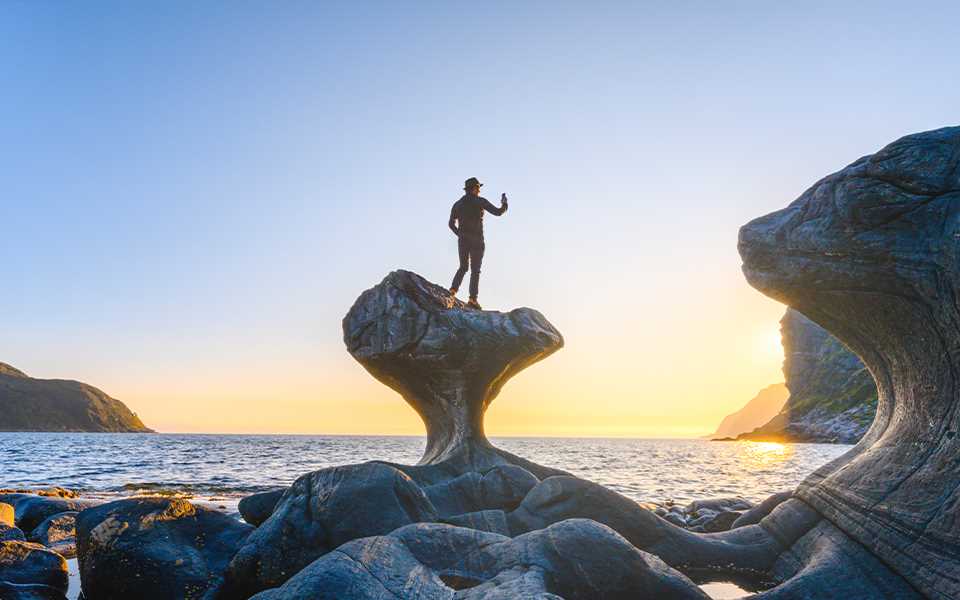 A man taking a photo of the sunset whilst standing on a rock formation by the sea