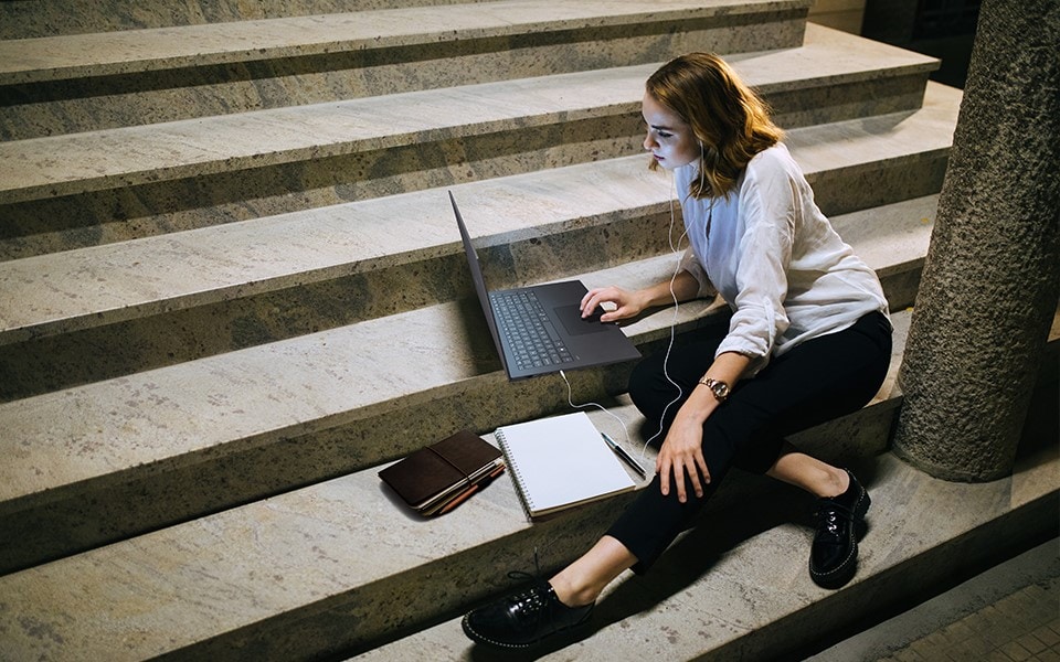 Kobieta siedzi na schodach na zewnątrz pracuje na swoim laptopie