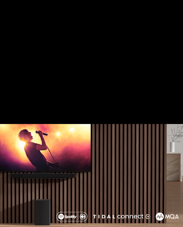 LG OLED C este așezat pe perete, dedesubt, bara de sunet LG SC9S este așezată prin intermediul unei console exclusive. Subwoofer-ul este așezat dedesubt. Pe televizor este prezentată o scenă de concert.