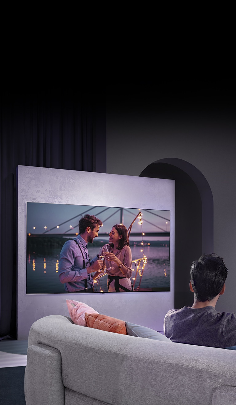 Osoba na pohovke sleduje film na veľkej obrazovke televízora na stene.