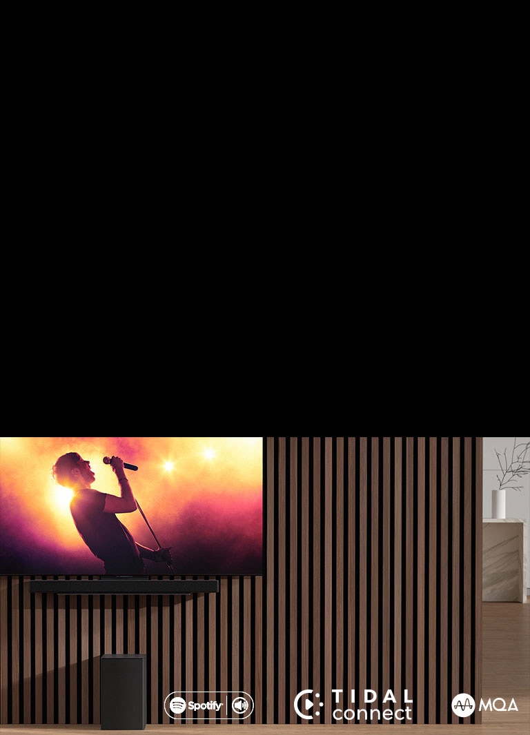 Model LG OLED C je umiestnený na stene. Pod ním je umiestnený zvukový panel LG SC9S prostredníctvom exkluzívnej konzoly. Nižšie sa nachádza subwoofer. Na obrazovke televízora sa zobrazuje scéna z koncertu.