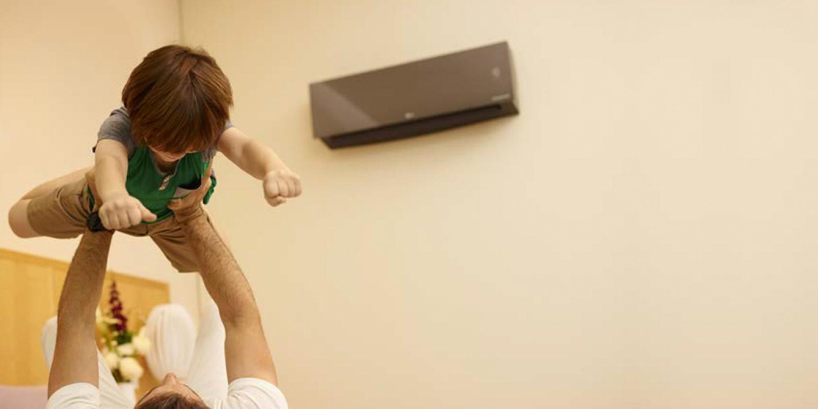 Man lifting a child up with a with an LG thru-the-wall air conditioner in the background.