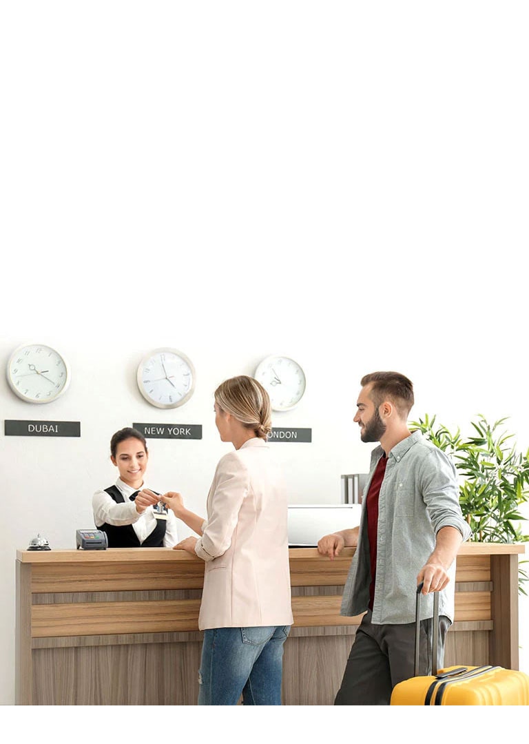 An image of a couple checking in with a receptionist at a hotel lobby.