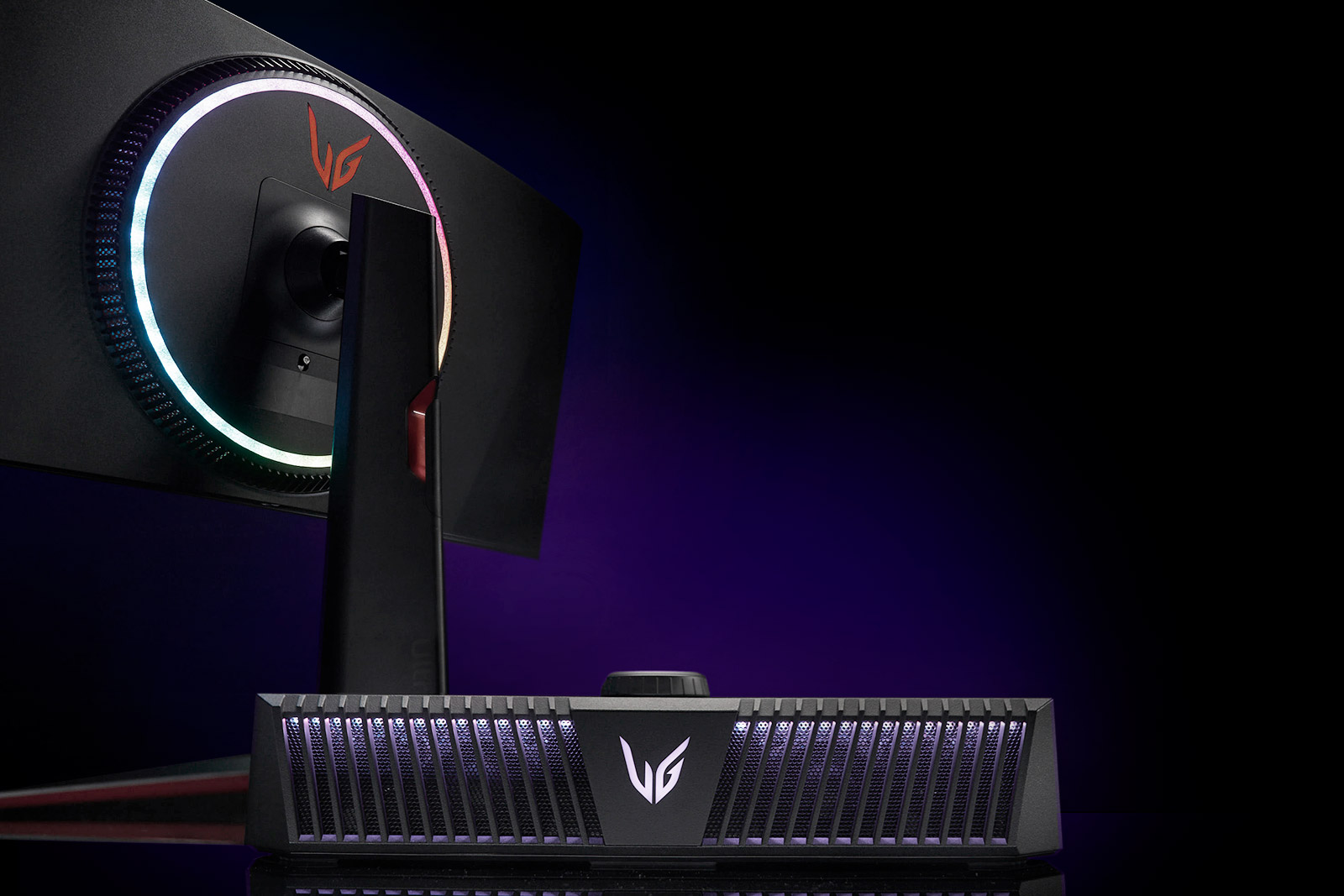 A back view of a gaming monitor and a front eye view of a gaming speaker with purple lighting