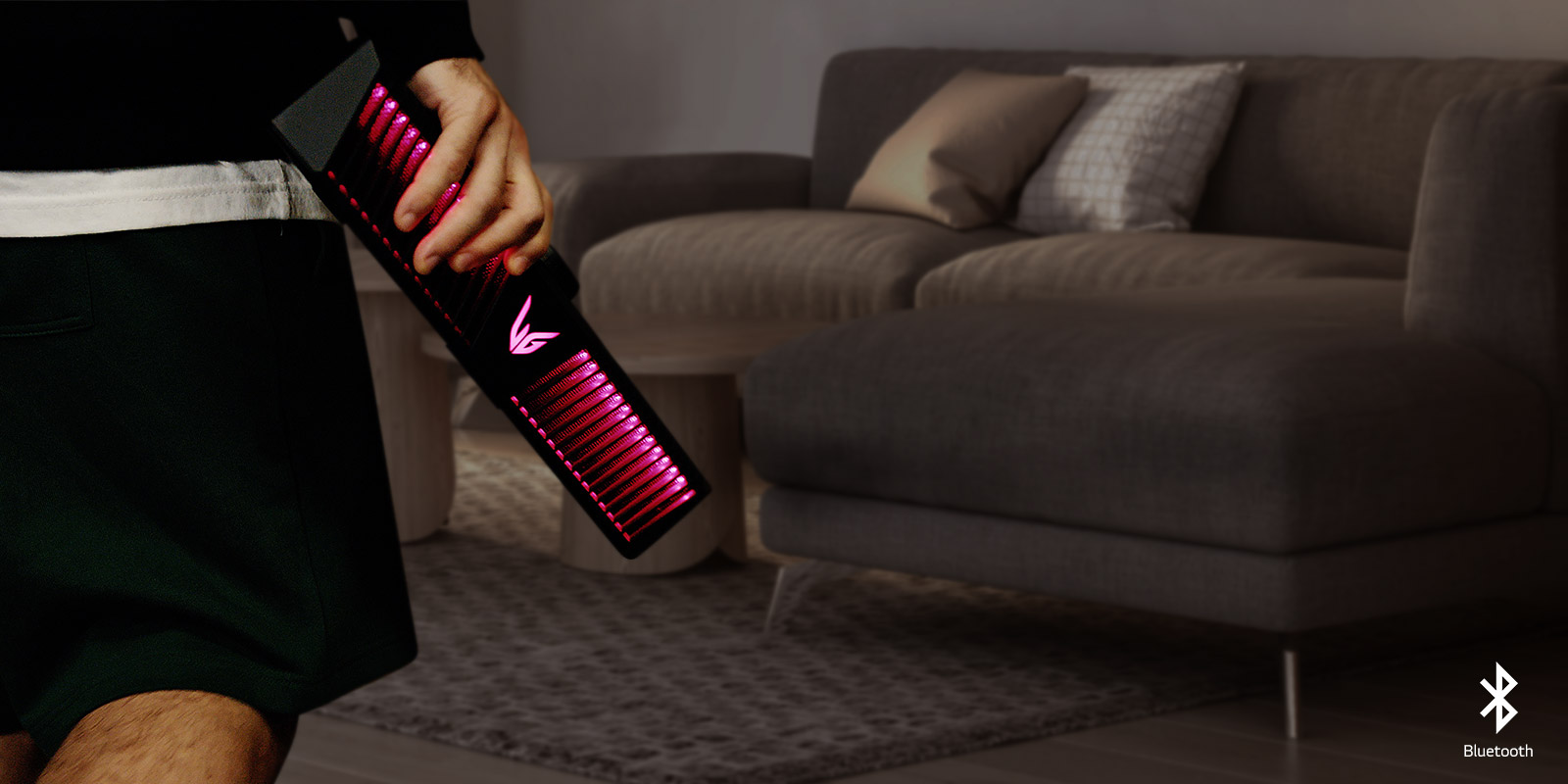 A man's hand holding the gaming speaker with pink lighting. There is a living room in the background.