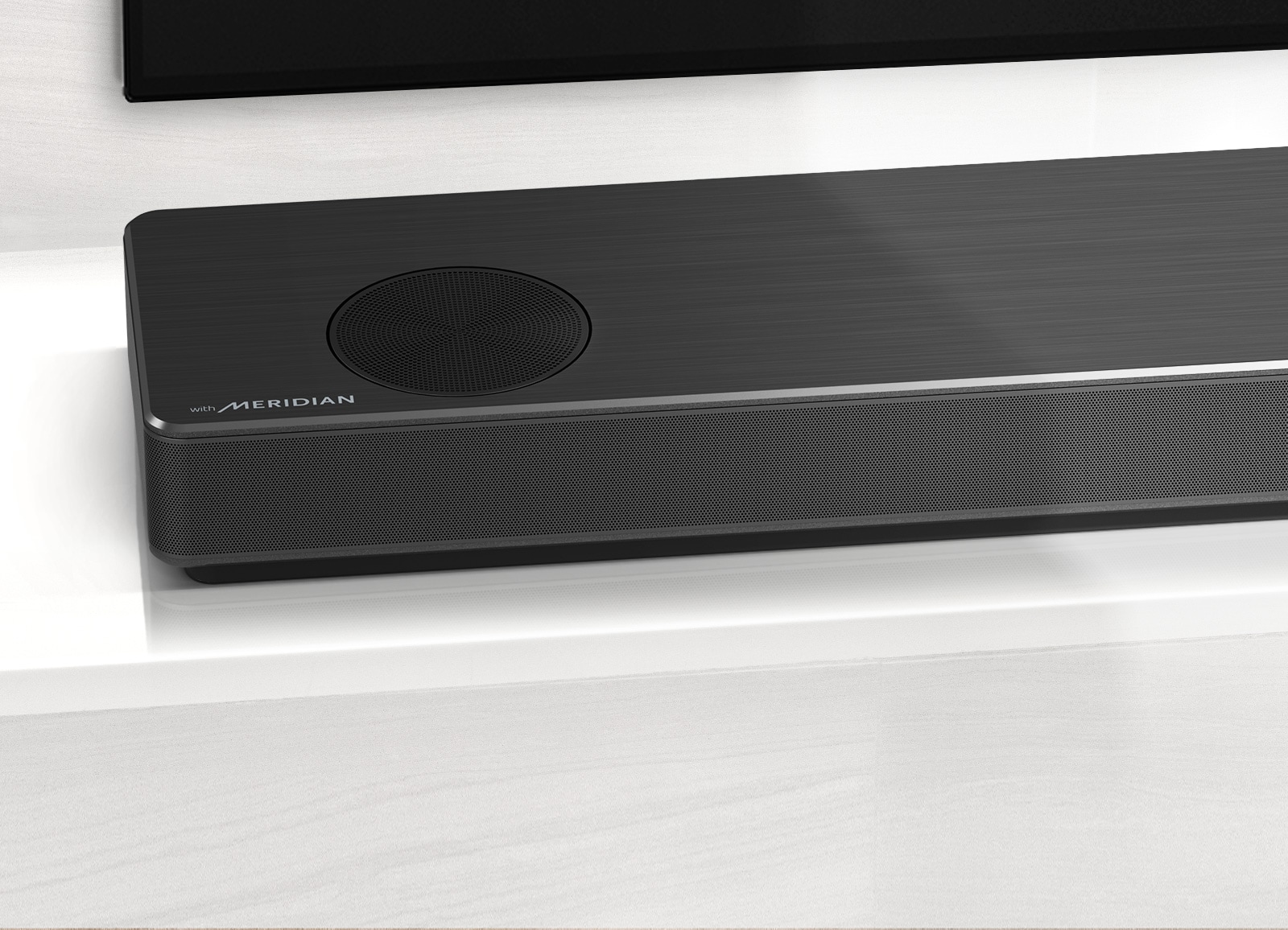 Close-up of LG Soundbar left side with Meridian logo shown on bottom left corner. Bottom left side of TV is also visible. 