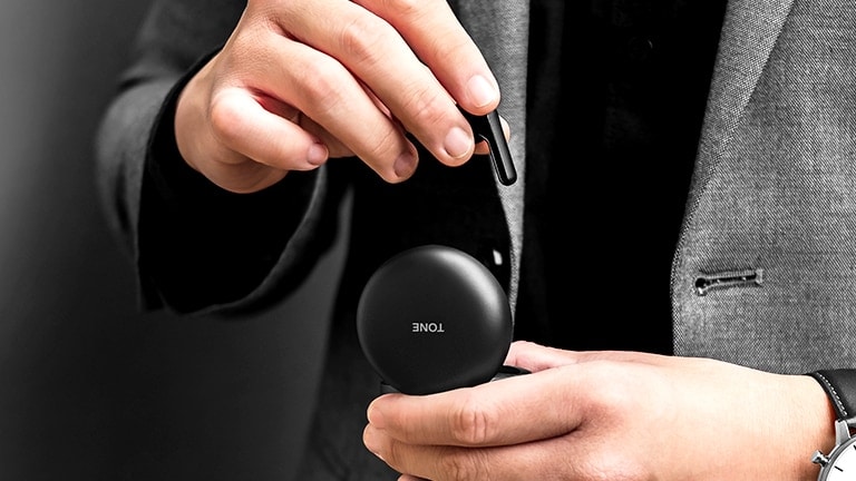 An image of a man dressed in grey suit holding a black LG TONE Free Fn4 cradle and taking out an earbud from it
