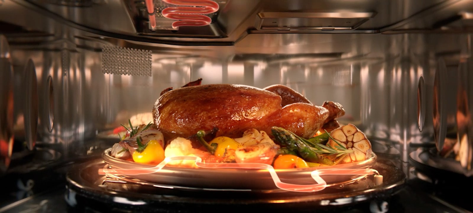 Whole chicken roasting on a rotating tray inside an LG SolarDOM, evenly cooked with surrounding vegetables.