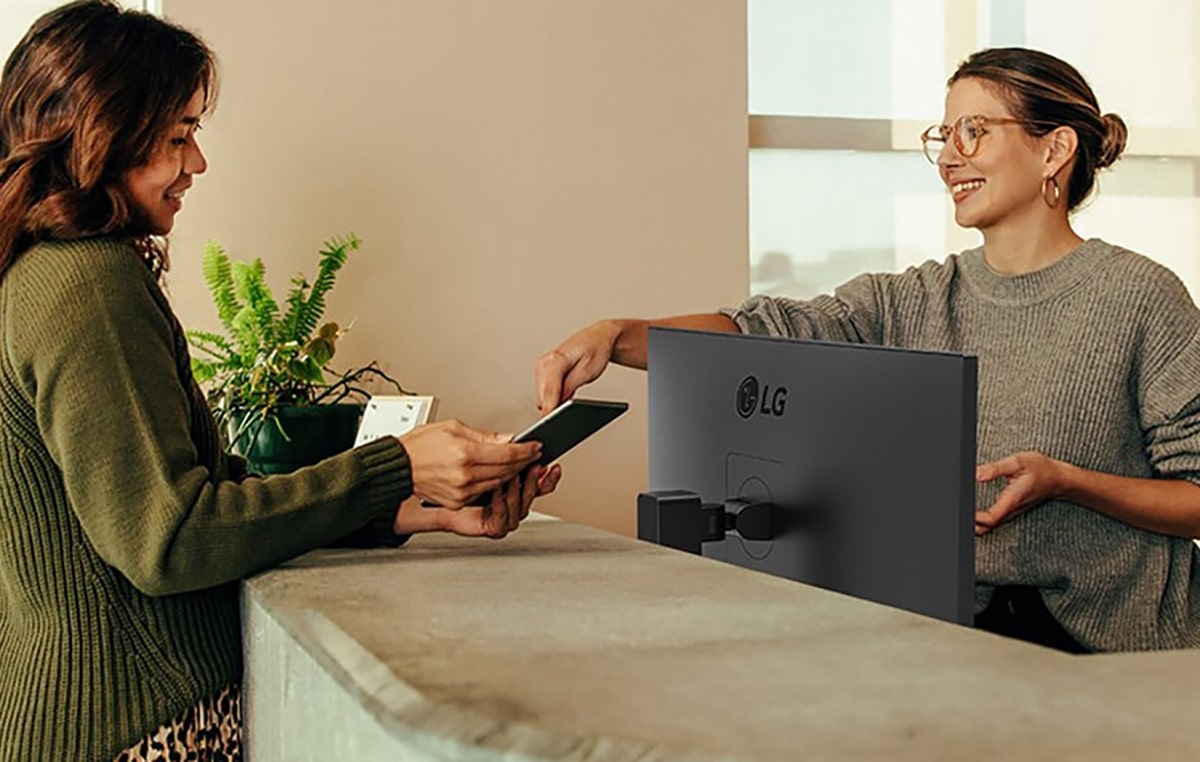 Friendly receptionist showing a woman where to sign on a digital tablet.	