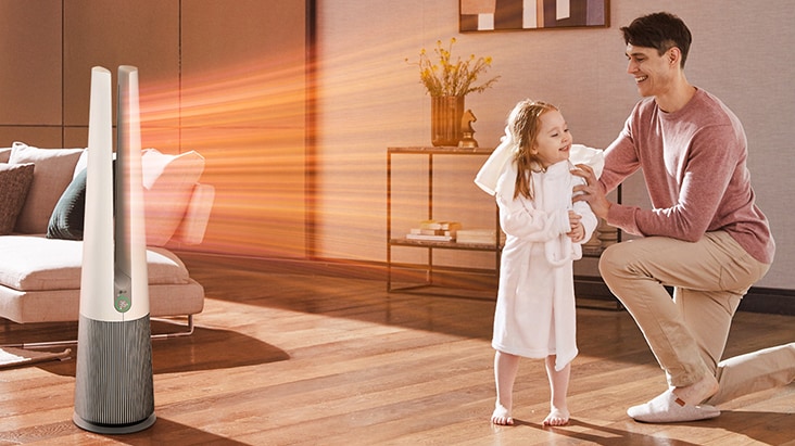 An air purifier blowing warm airflow toward a child in a bathrobe and a man smiling in a living room.