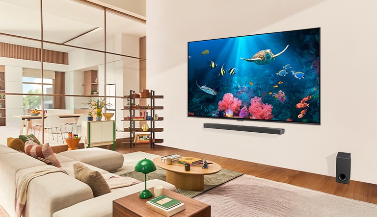 A family in a living room with an ultra big LG TV mounted on the wall, with an ocean scene including coral and a turtle on the screen.