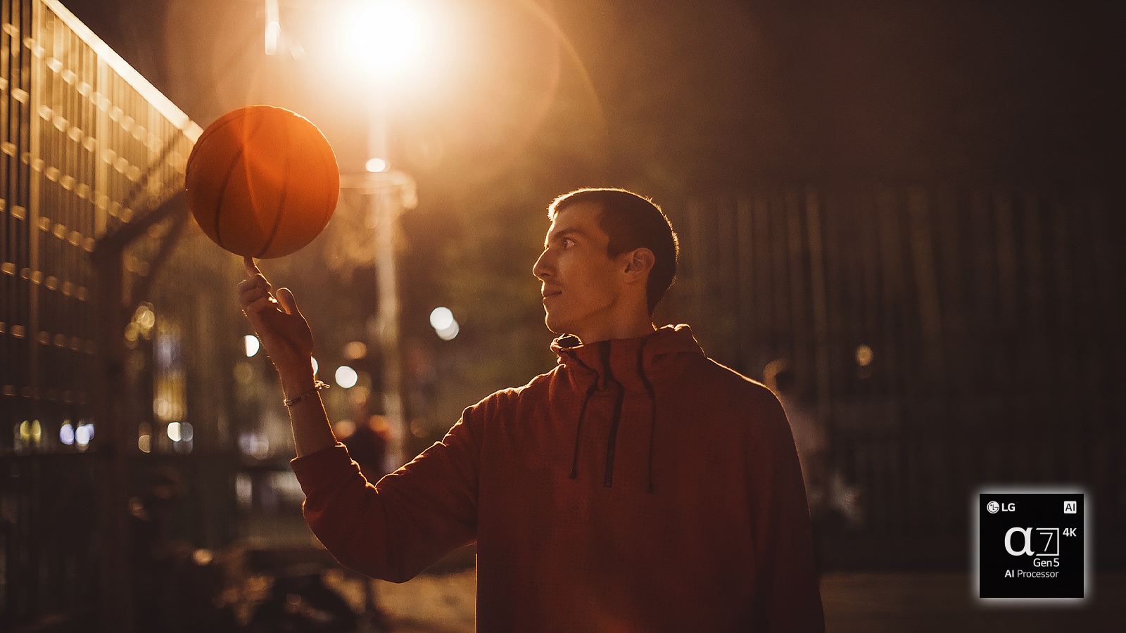 A man in a basketball court at night spins a basketball on his finger.