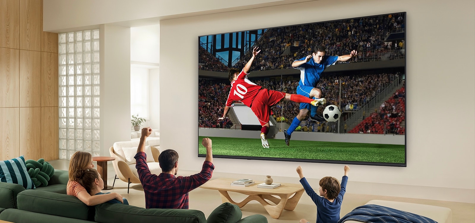 LG QNED AI QNED70 Mini LED Ultra Big TV is wall-mounted in a bright living room, showing an intense soccer moment with vivid colors and refined picture quality across a wide screen, as a family seated on sofas cheers together.