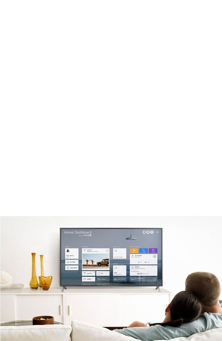 A men and women sitting on a sofa in the living room with the Home Dashboard on the TV screen.