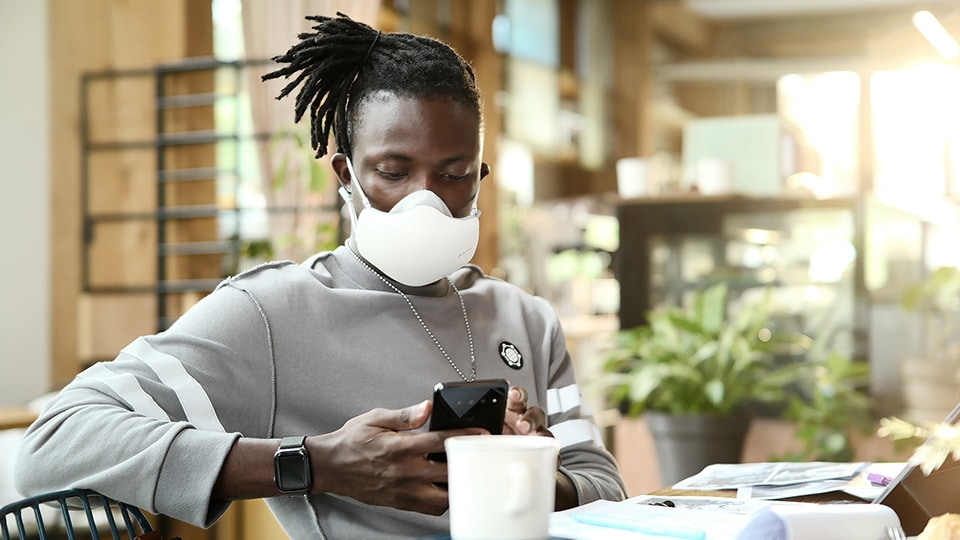 An African American man is looking at his cell phone, with a balck LG PuriCare™ Wearable Air Purifier on.
