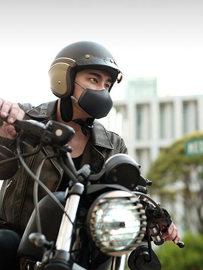 An Asian man is riding a motorcycle, with a black LG PuriCare™ Wearable Air Purifier on.