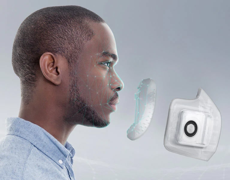 The side of a man's face is shown with dots and lines mapped on to his face. In front of his face is the interior part of the Wearable Air Purifier and then the exterior Wearable Air Purifier indicating that it fits comfortably and seals to his face.