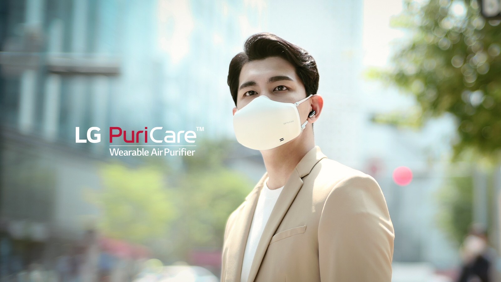A man stands downtown in a city with the LG PuriCare wearable Air Purifier on, looking around with a blurred city in the background.