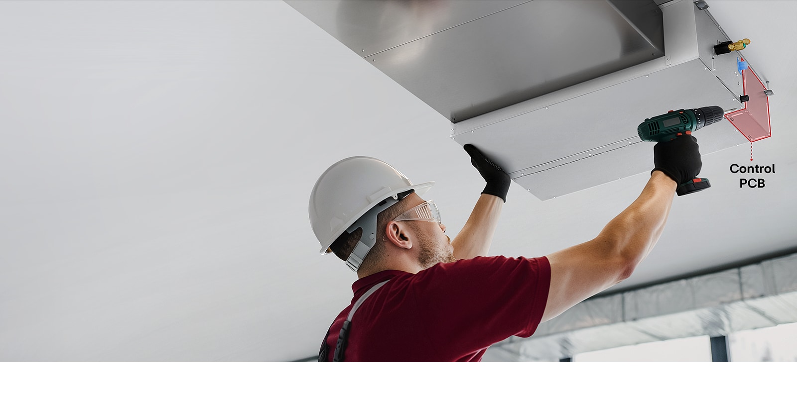 A technician servicing a Ceiling Concealed Ducted Unit, accessing the control PCB through a bottom panel using a power drill.