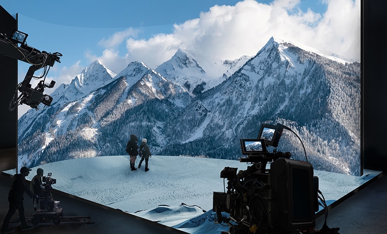 A virtual production studio with curved LED walls and ceiling and floor LEDs is filming a video of snowy mountain scenery.
