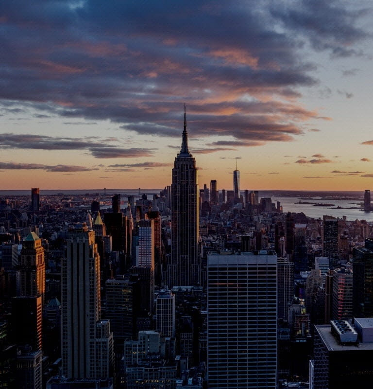 From a lofty vantage point, the New York City skyline unfurls under a sky ablaze with the crimson glow of the setting sun.