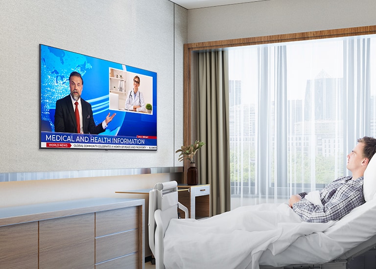 The patient is lying in the hospital room’s bed and watching the TV hanging on the wall.